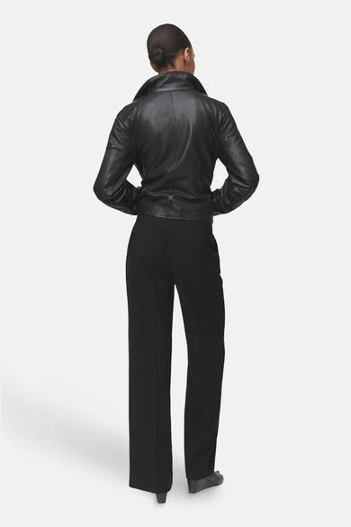 Pantalon noir de MANGO, coupe droite et ample, porté avec une veste en cuir noir.