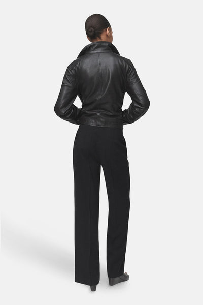 Pantalon noir de MANGO, coupe droite et ample, porté avec une veste en cuir noir.