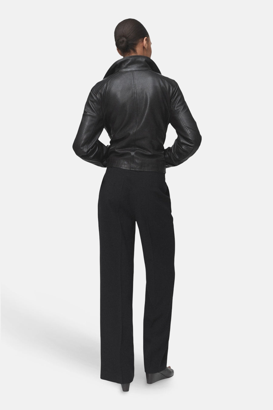 Pantalon noir de MANGO, coupe droite et ample, porté avec une veste en cuir noir.