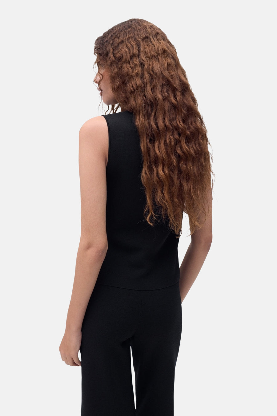 Chemisier sans manches noir de MANGO, avec une texture lisse, porté avec un pantalon noir assorti.