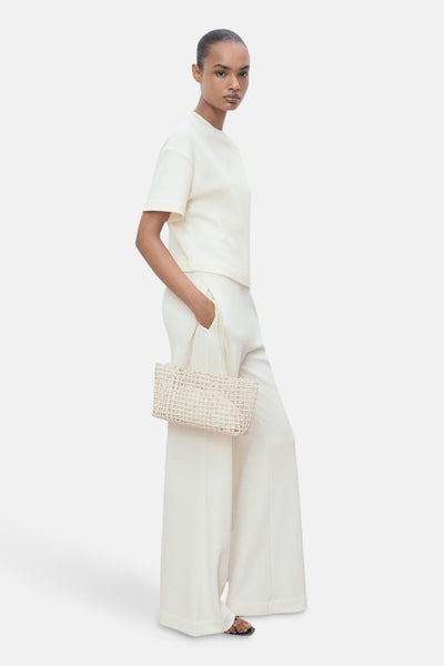 Pantalon blanc de MANGO, ample et taille haute, porté avec un t-shirt crème et un sac à main en osier.
