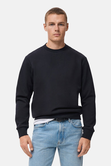 Blauwe trui van MANGO, gedragen over een wit T-shirt met een spijkerbroek en een zwarte riem.