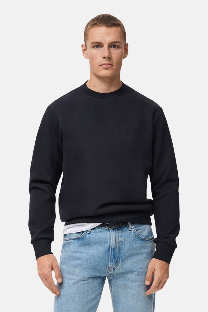 Blauwe trui van MANGO, gedragen over een wit T-shirt met een spijkerbroek en een zwarte riem.