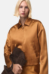 Gilet marron de MANGO avec une texture satinée et un sac à main en daim dans la main.