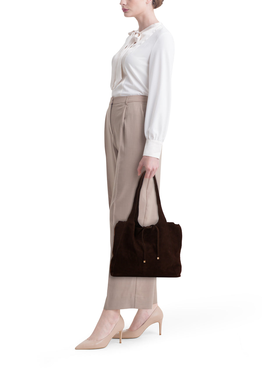 Sac à main brun en daim de MANGO, porté avec un pantalon beige et des escarpins nude.
