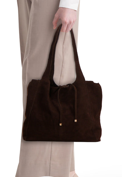 Sac à main brun de MANGO, avec cordon de serrage en daim et détails dorés, porté avec un pantalon beige.