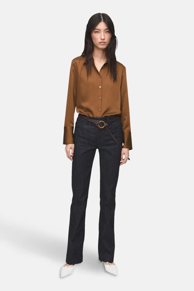 Chemise à manches longues brune de MANGO, portée avec un pantalon bleu foncé et une ceinture marron.