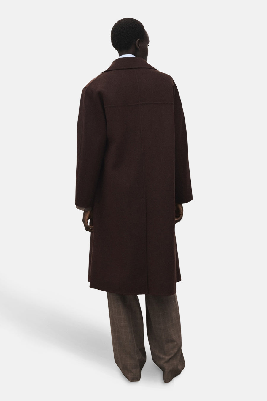 Veste longue brun de MANGO, vue de dos, portée avec un pantalon à carreaux.