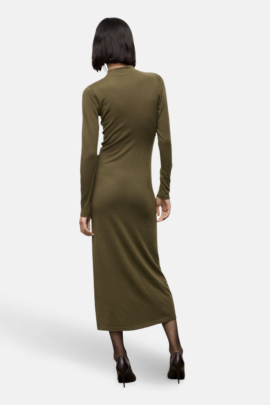 Robe longue kaki à manches longues de MANGO, avec une texture douce et des collants noirs et des escarpins marron.
