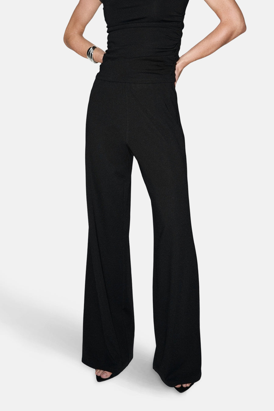 Pantalon noir de MANGO, à jambes larges, porté avec un haut noir et des accessoires argentés.
