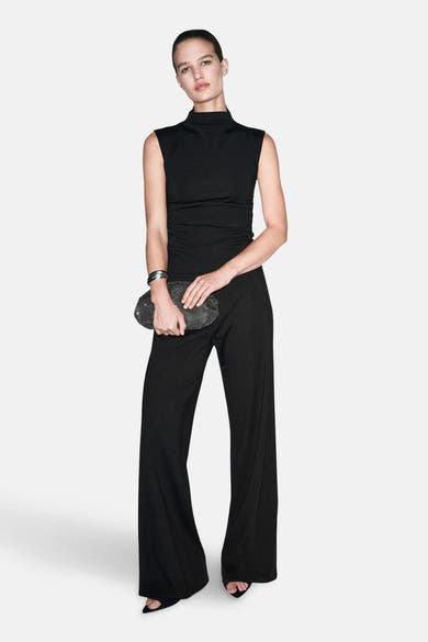 Pantalon noir de MANGO, jambe large, porté avec un haut noir sans manches et une pochette noire.