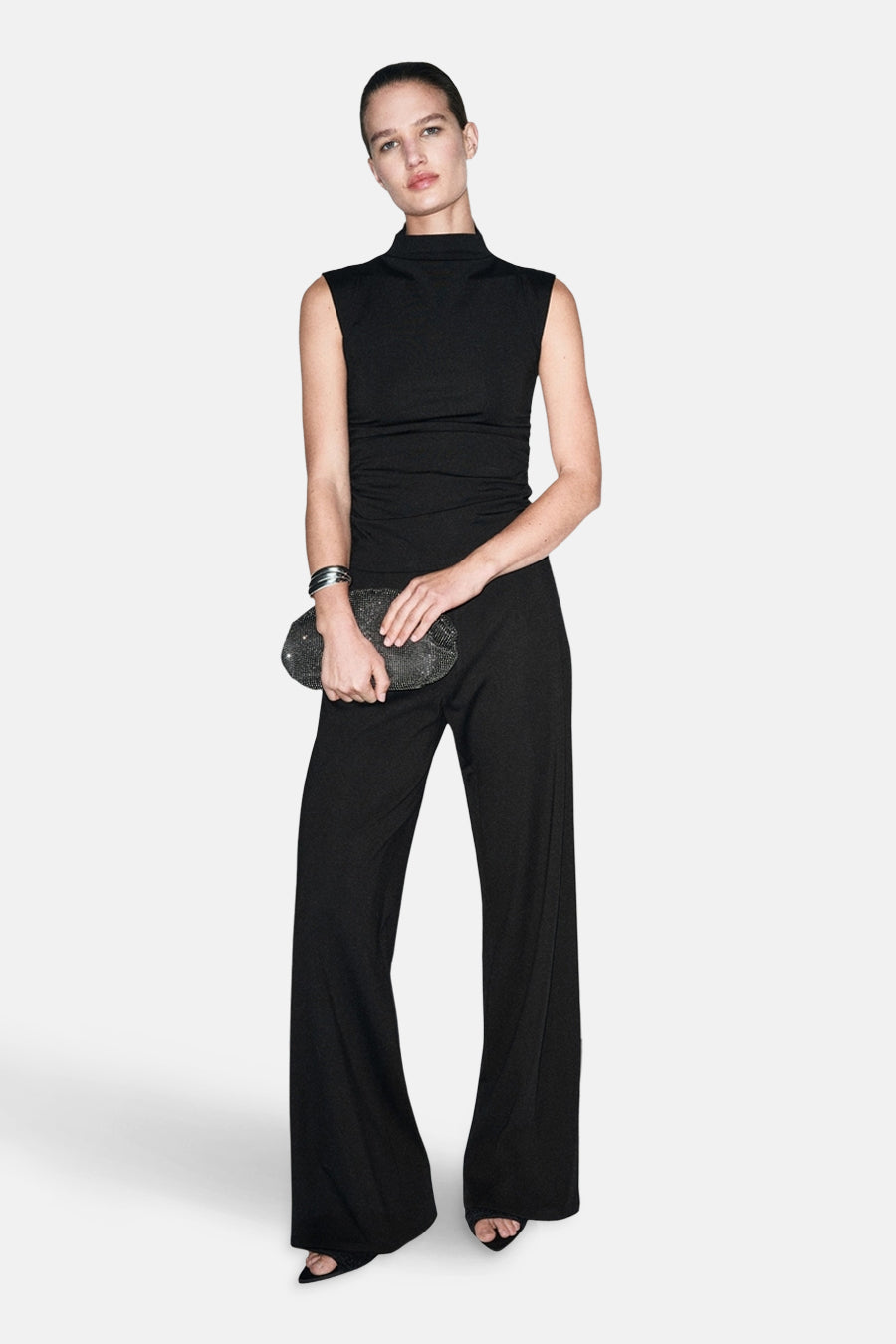Pantalon noir de MANGO, jambe large, porté avec un haut noir sans manches et une pochette noire.