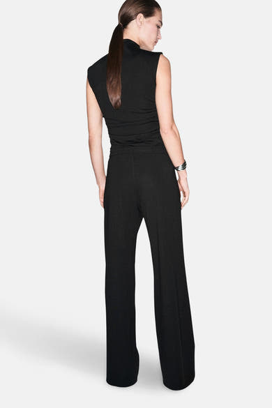 Pantalon noir par MANGO, jambe large et fluide, porté avec un haut noir sans manches et un bracelet argenté.