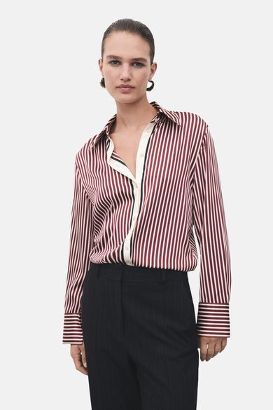 Chemise à rayures rouge de MANGO, avec une patte de boutonnage crème à bordure noire, portée avec un pantalon noir rayé.
