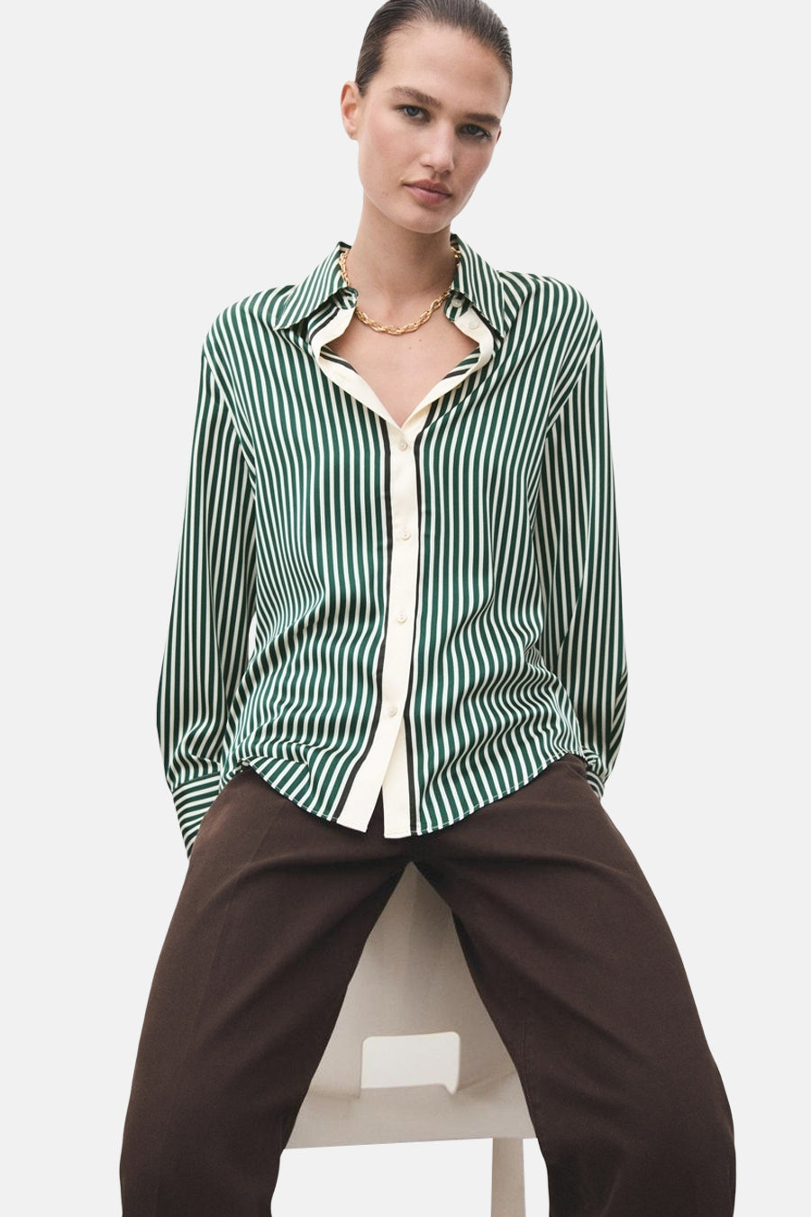 Chemisier à manches longues vert rayé de MANGO, porté avec un pantalon marron et un collier doré.
