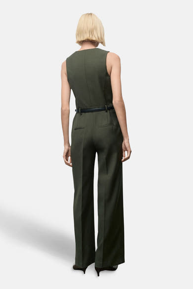 Combinaison kaki de MANGO, avec ceinture noire fine, coupe large et poches arrière passepoilées.