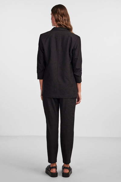 Blazer noir par PIECES® avec manches trois-quarts, vu de dos, porté avec un pantalon assorti et des sandales plateforme.