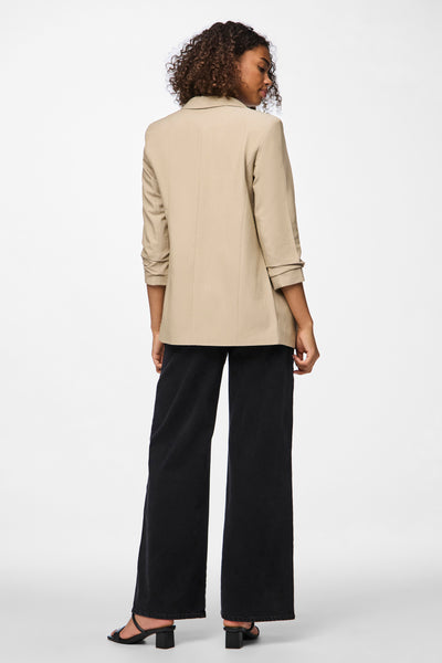 Blazer beige de PIECES®, porté avec un pantalon noir ample et des talons.
