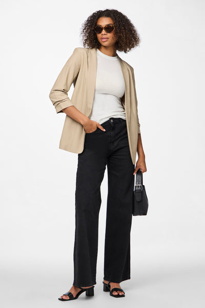 Beige blazer van PIECES®, gedragen met een wit T-shirt, een zwarte jeans en zwarte sandalen met hak.
