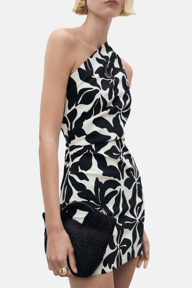 Zwarte jurk met grafische bloemenprint van MANGO, met een asymmetrische snit en een gevlochten zwarte clutch.