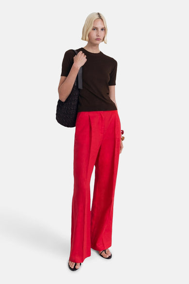 T-shirt à manches courtes brun de MANGO, porté avec un pantalon rouge ample et un sac à bandoulière noir.
