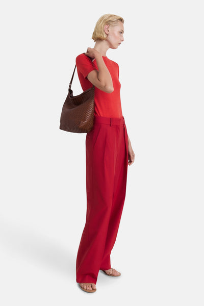 T-shirt rouge à manches courtes de MANGO, porté avec un pantalon rouge ample et un sac tressé marron.