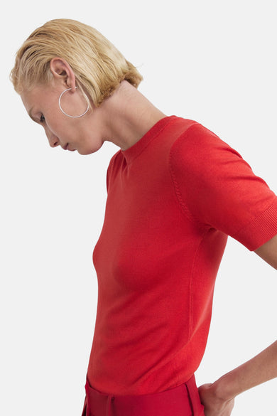 T-shirt rouge à manches courtes de MANGO, porté avec des boucles d'oreilles argentées et un pantalon assorti.