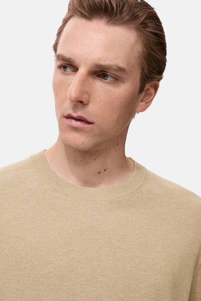 Pull à col rond beige de MANGO, en maille fine texturée, porté par un homme regardant vers la gauche.
