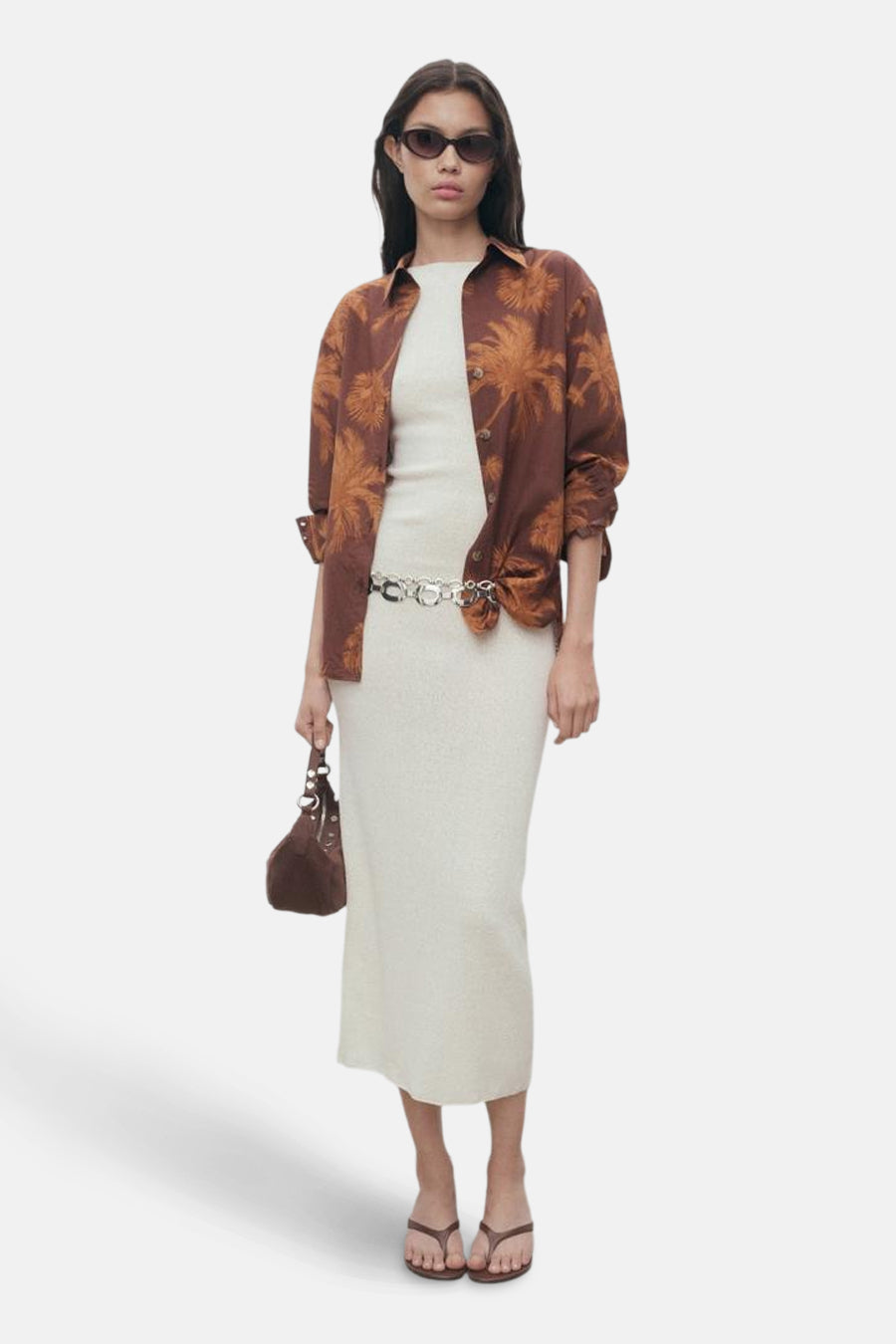 Bruin overhemd met lange mouwen en palmboomprint van MANGO, gedragen open over een witte jurk met een zilveren riem.