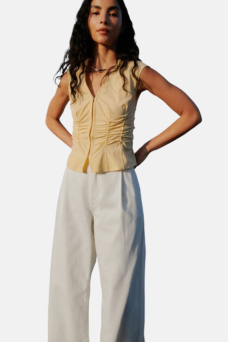 Gele mouwloze blouse van MANGO, met geplooide details aan de voorkant, gedragen met een witte broek.