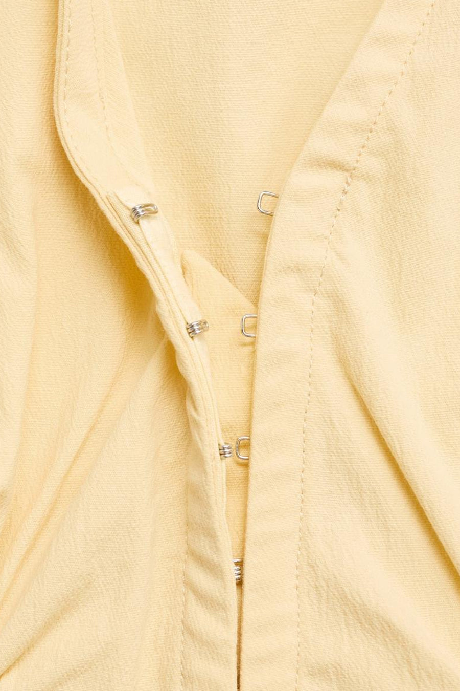 Gele blouse van MANGO met zilverkleurige haaksluiting, lichte textuur en stikseldetails.