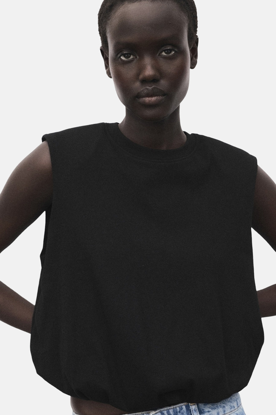 Top sans manches noir de MANGO, porté avec un jean taille basse, posant sur un fond clair.

