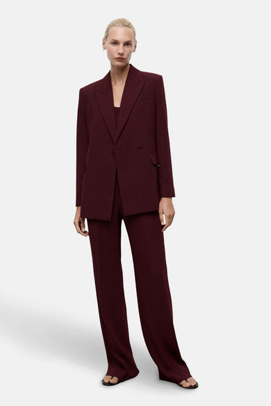 Blazer bordeaux par MANGO, coupe droite, porté avec un pantalon assorti et des chaussures ouvertes.