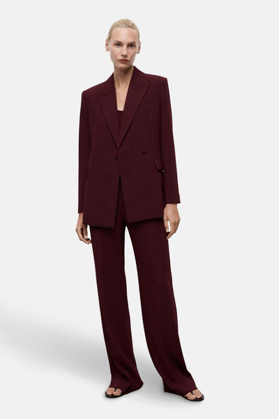 Blazer bordeaux par MANGO, coupe droite, porté avec un pantalon assorti et des chaussures ouvertes.