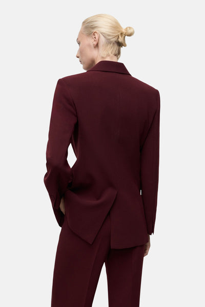 Blazer bordeaux de MANGO, porté avec un pantalon assorti, vu de dos, avec un chignon blond.