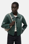 Veste courte verte de MANGO, portée avec un sac beige et un jean noir taille haute.
