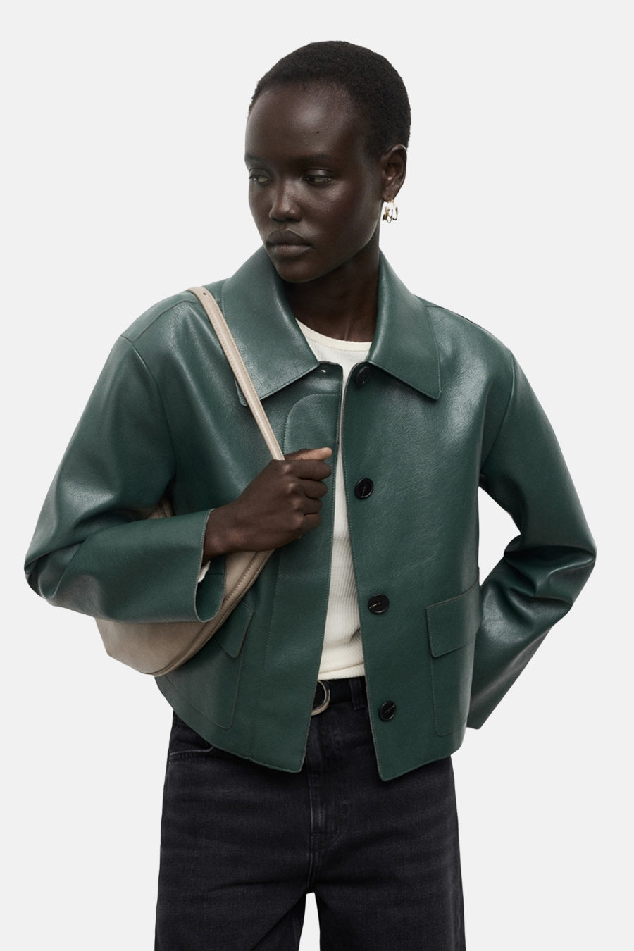 Veste courte verte de MANGO, portée avec un sac beige et un jean noir taille haute.
