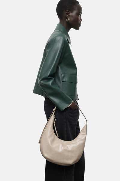 Korte groene jas van MANGO, met een gladde textuur en een getailleerde kraag, gedragen met een beige handtas en een zwarte jeans.
