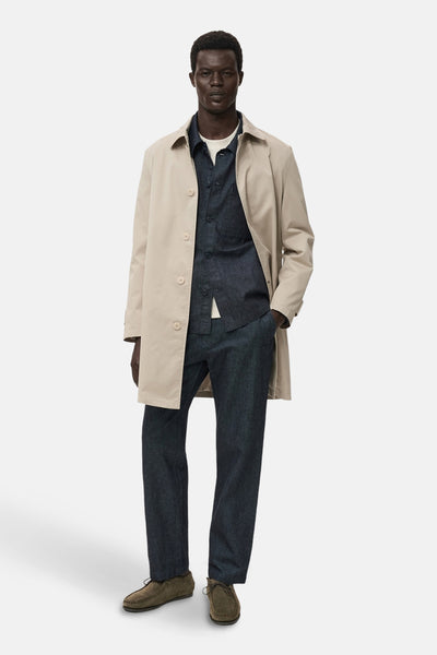 Veste en jean bleu foncé de MANGO, portée sur un t-shirt blanc avec un pantalon assorti et un manteau beige.
