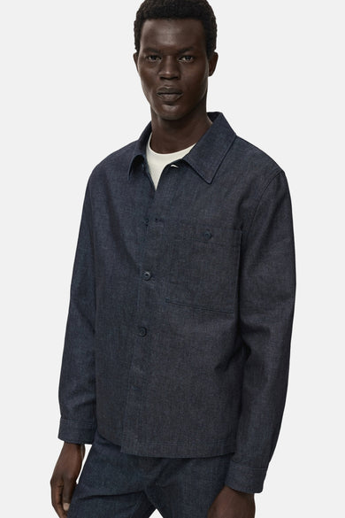 Veste en jean bleu foncé de MANGO, avec poche poitrine et boutons ton sur ton, portée sur un t-shirt blanc.