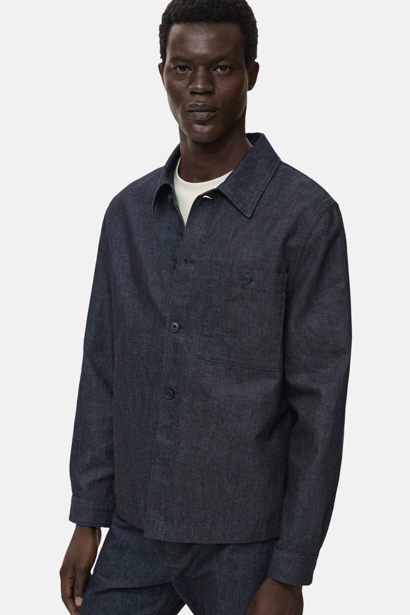 Veste en jean bleu foncé de MANGO, avec poche poitrine et boutons ton sur ton, portée sur un t-shirt blanc.