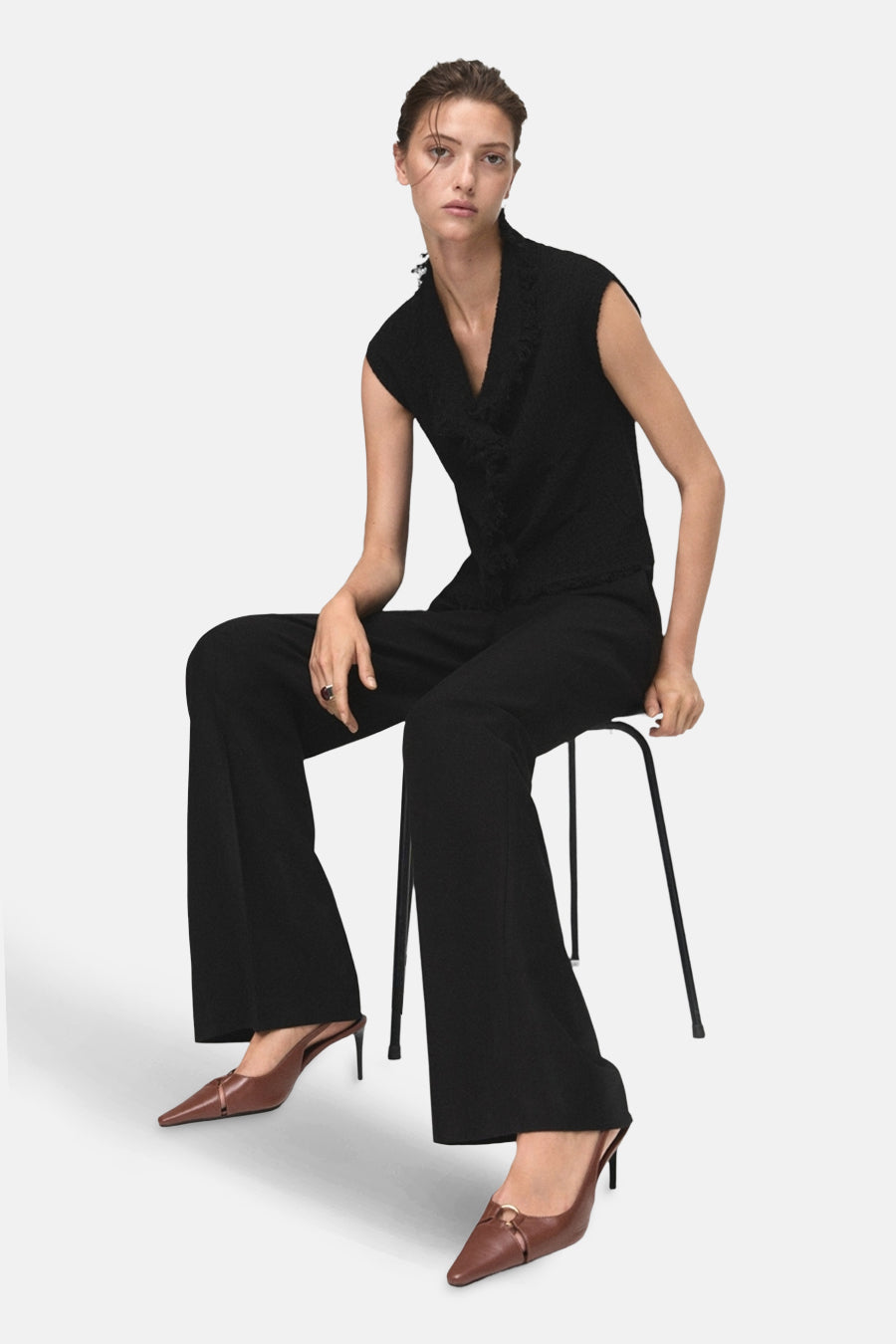 Débardeur noir de MANGO, avec col en V et détail texturé, porté avec un pantalon noir et des escarpins marron.