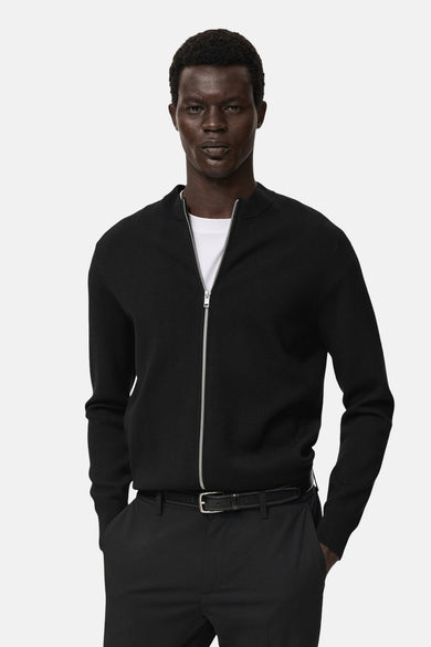 Zwart gilet van MANGO gedragen over een wit T-shirt, met ritssluiting en zwarte broek.