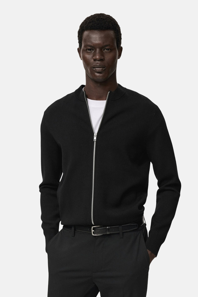 Zwart gilet van MANGO gedragen over een wit T-shirt, met ritssluiting en zwarte broek.