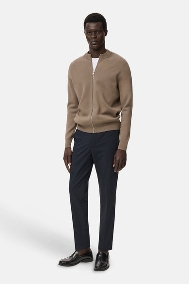 Bruin vest met rits van MANGO, gedragen over een wit T-shirt en een marineblauwe pantalon met zwarte loafers.