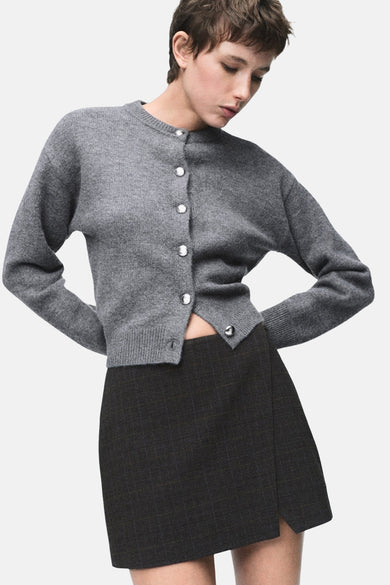 Gilet gris de MANGO avec boutons argentés, porté sur une jupe à carreaux foncée.
