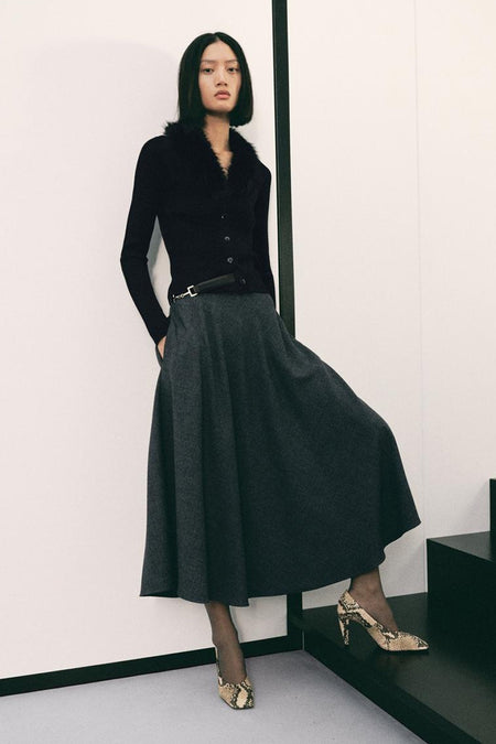 Cardigan noir à garniture en fourrure de MANGO, porté avec une jupe longue grise et des escarpins imprimés.
