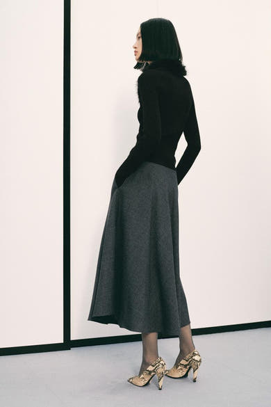Cardigan noir à col fourrure de MANGO, porté avec une jupe grise et des escarpins imprimés peau de serpent.