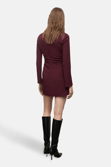 Robe bordeaux à manches longues de MANGO, vue de dos, portée avec des bottes hautes noires.
