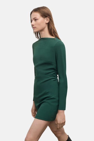 Groene jurk met lange mouwen van MANGO, gedragen met hoge zwarte laarzen met hak.